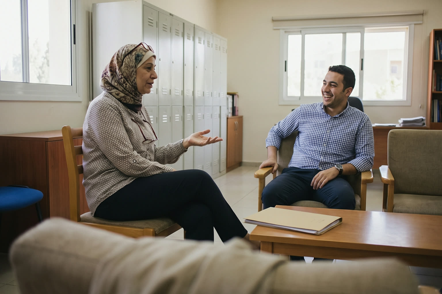 A senior teacher telling a young colleague something that makes him laugh in the staff room